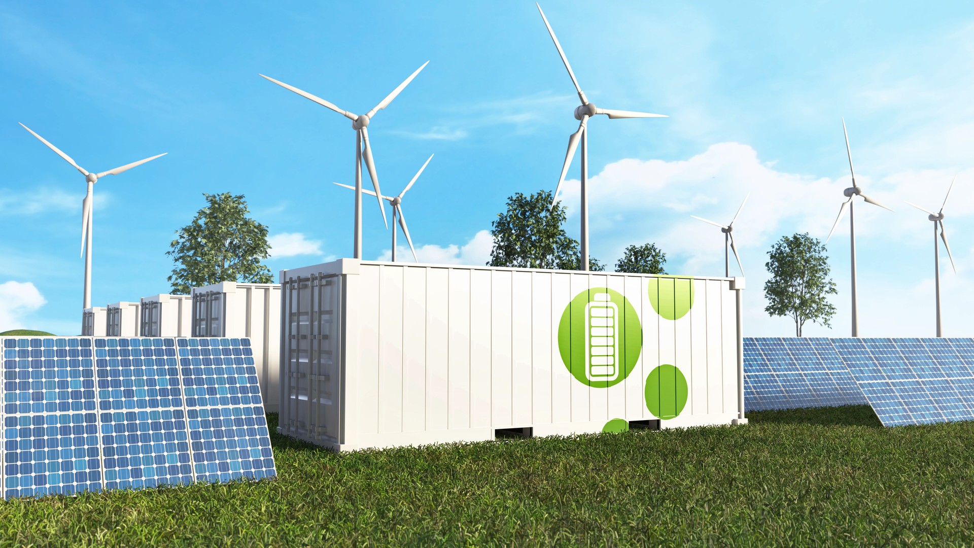 A row of battery storage containers sits in a field of solar panels and wind turbines